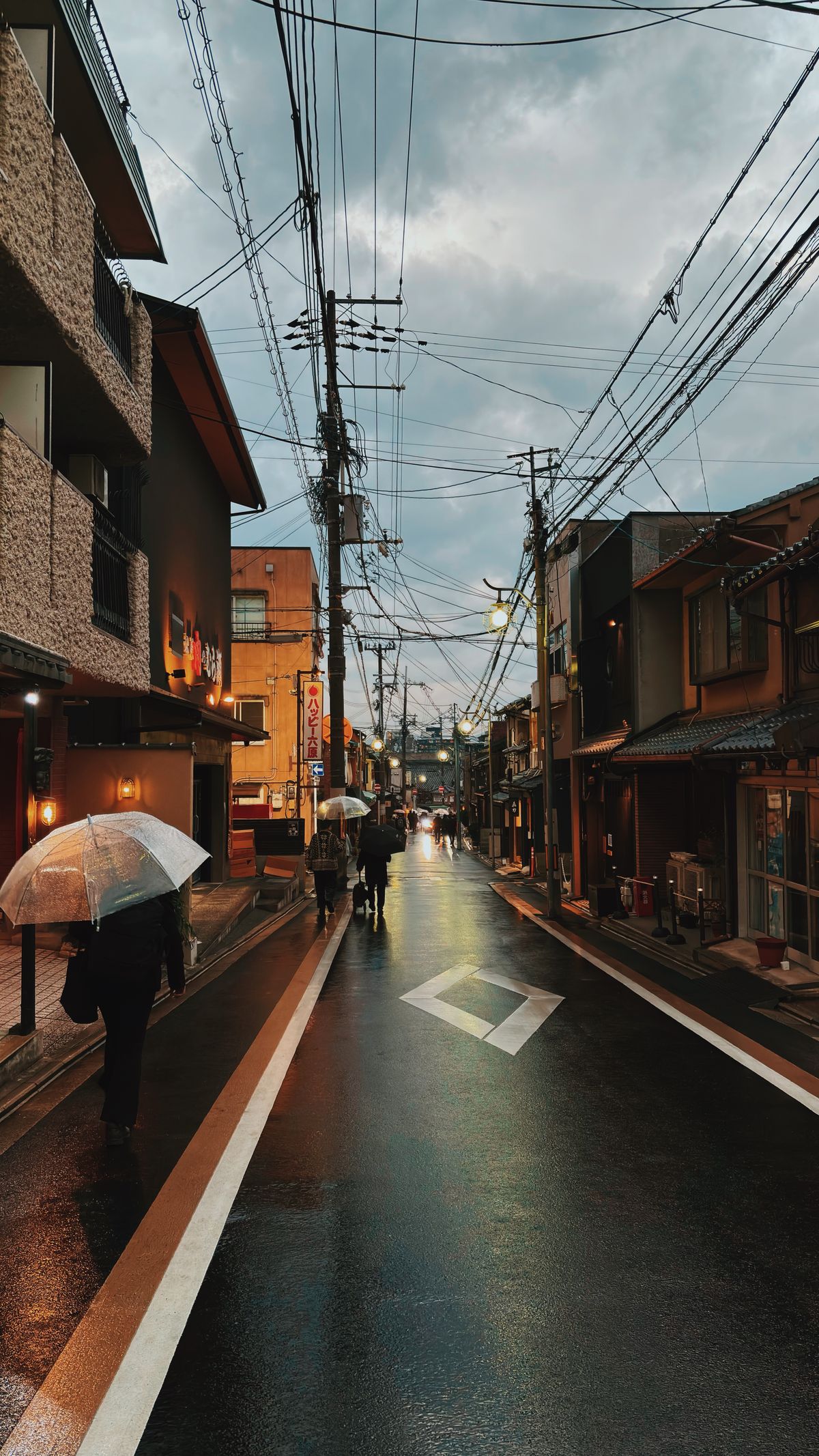 雨の夕暮れに傘をさして歩く人と濡れた道路