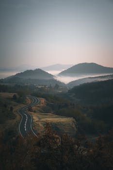 A winding road through misty mountains at dawn, creating a tranquil and scenic landscape.