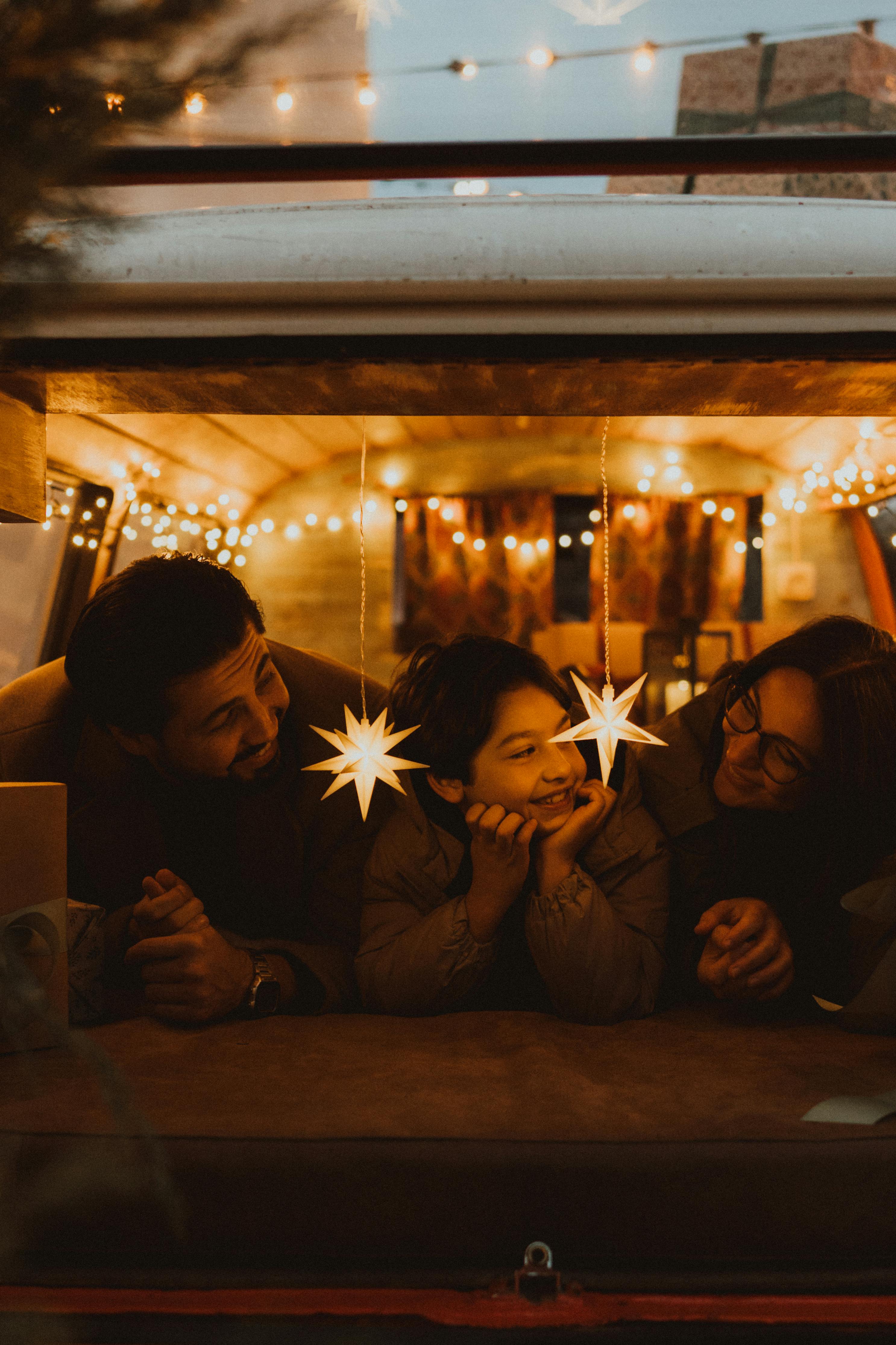 A family enjoys a warm moment with star lights inside a decorated camper van.