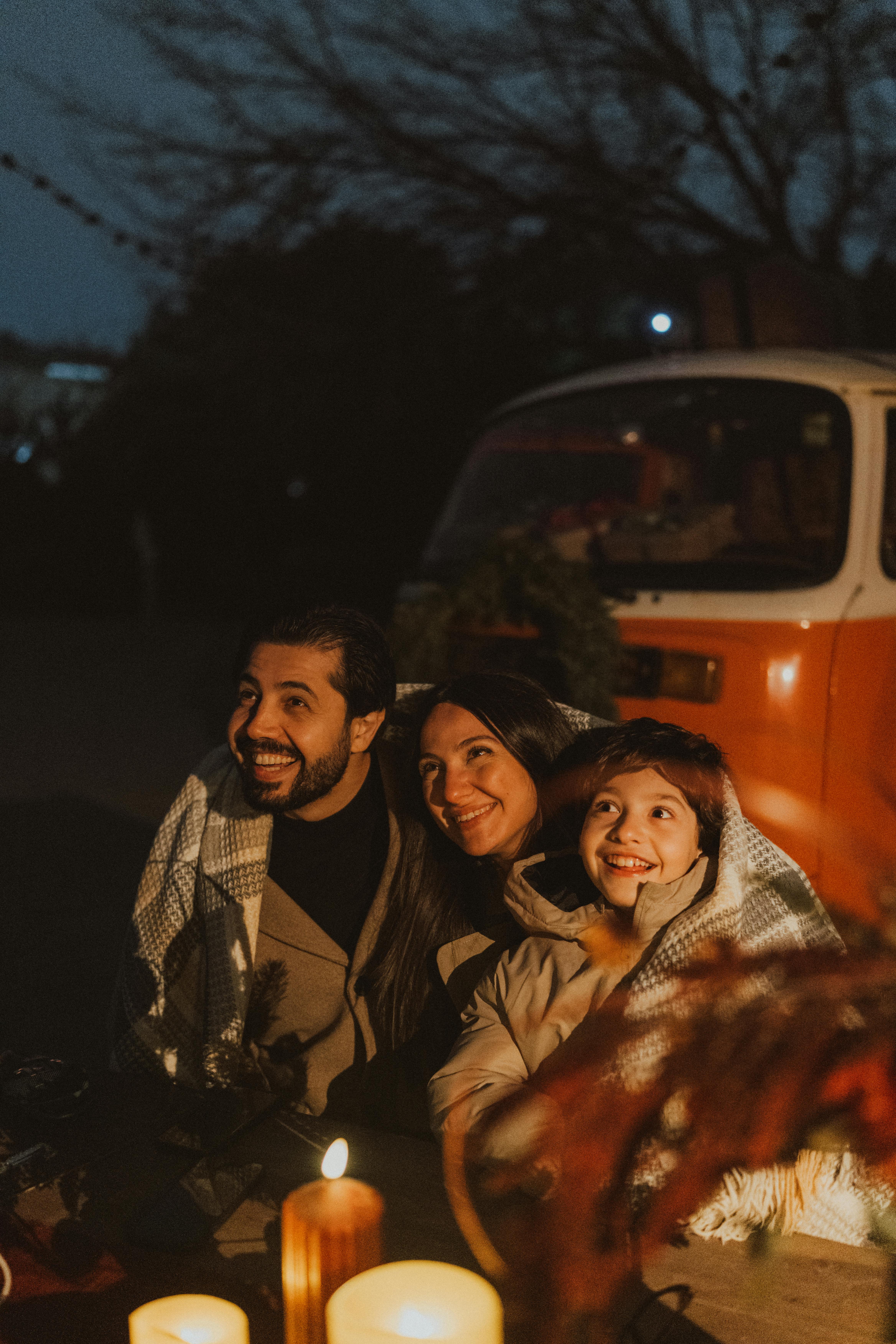 Family enjoying a cozy evening by candlelight near a camper van.