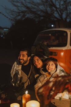 Family enjoying a cozy evening by candlelight near a camper van.