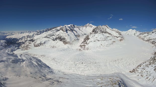 Stunning drone shot of a snow-covered glacier in the Swiss Alps under a clear blue sky.