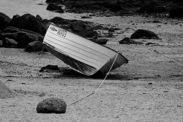 Black and white photo of an abandoned rowboat on a rocky shoreline, emphasizing solitude