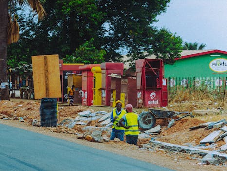 Operai con giubbotti catarifrangenti in un cantiere edile all'aperto con cabine telefoniche.