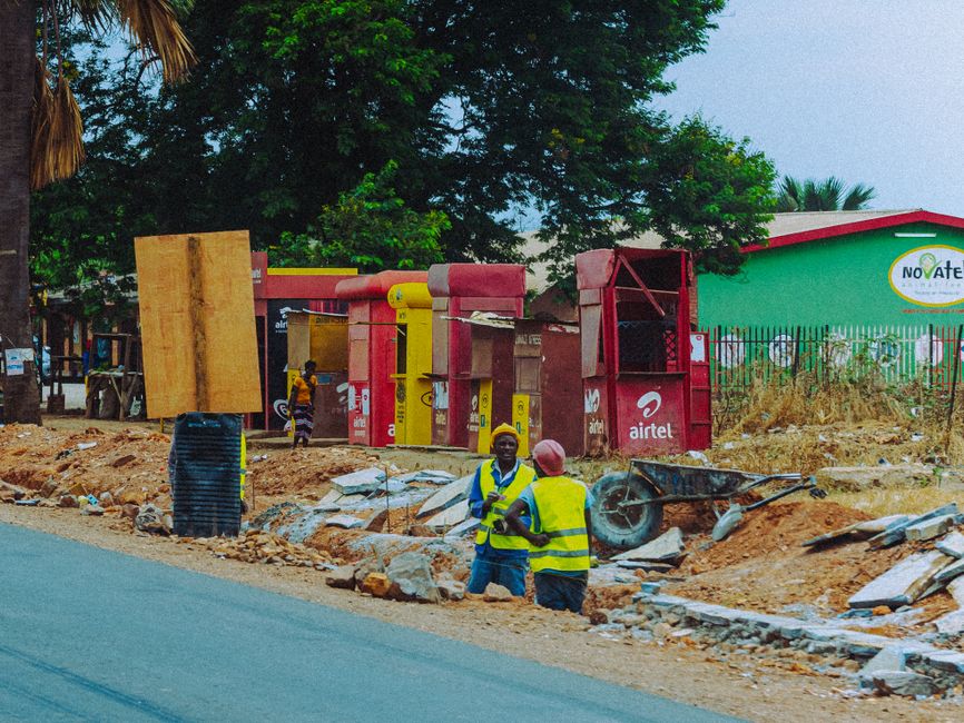 Workers in reflective vests at an outdoor construction site with phone booths.