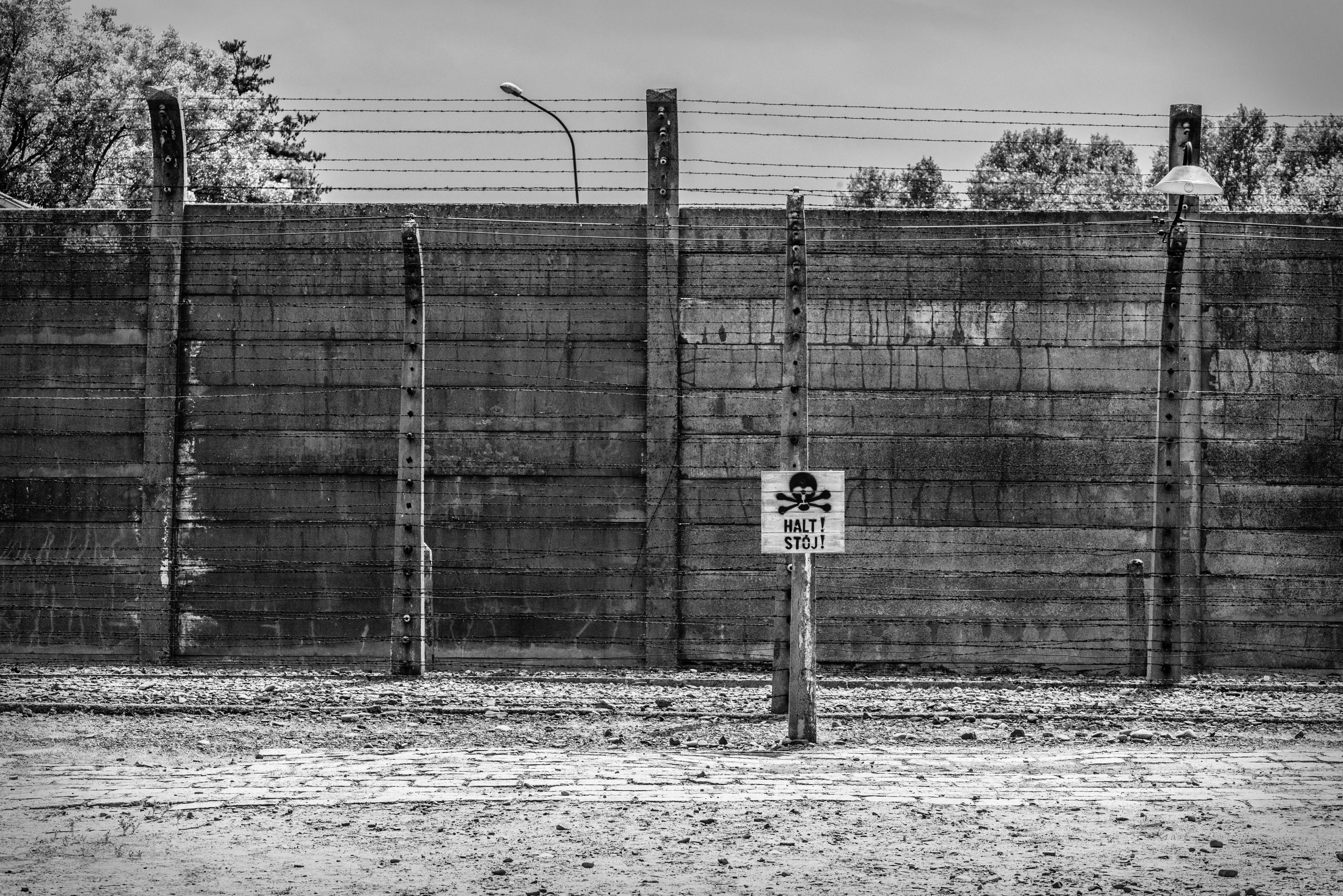 Monochrome image of Auschwitz Birkenau fence with warning sign in Poland.