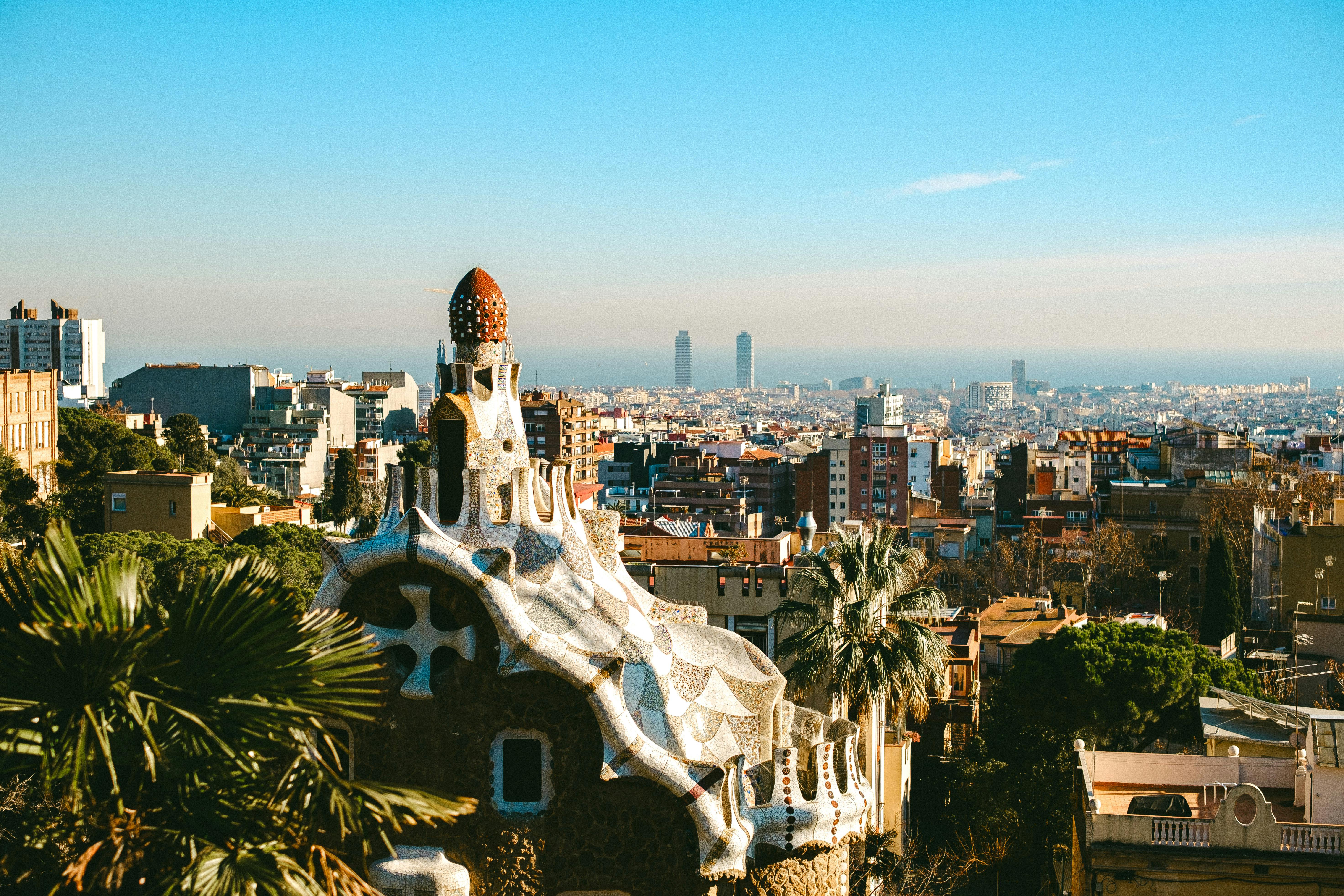 Panoramic view of Barcelona from Park Güell showing Gaudí's colorful ceramic mosaic work in the foreground with the city skyline and Mediterranean Sea stretching into the distance