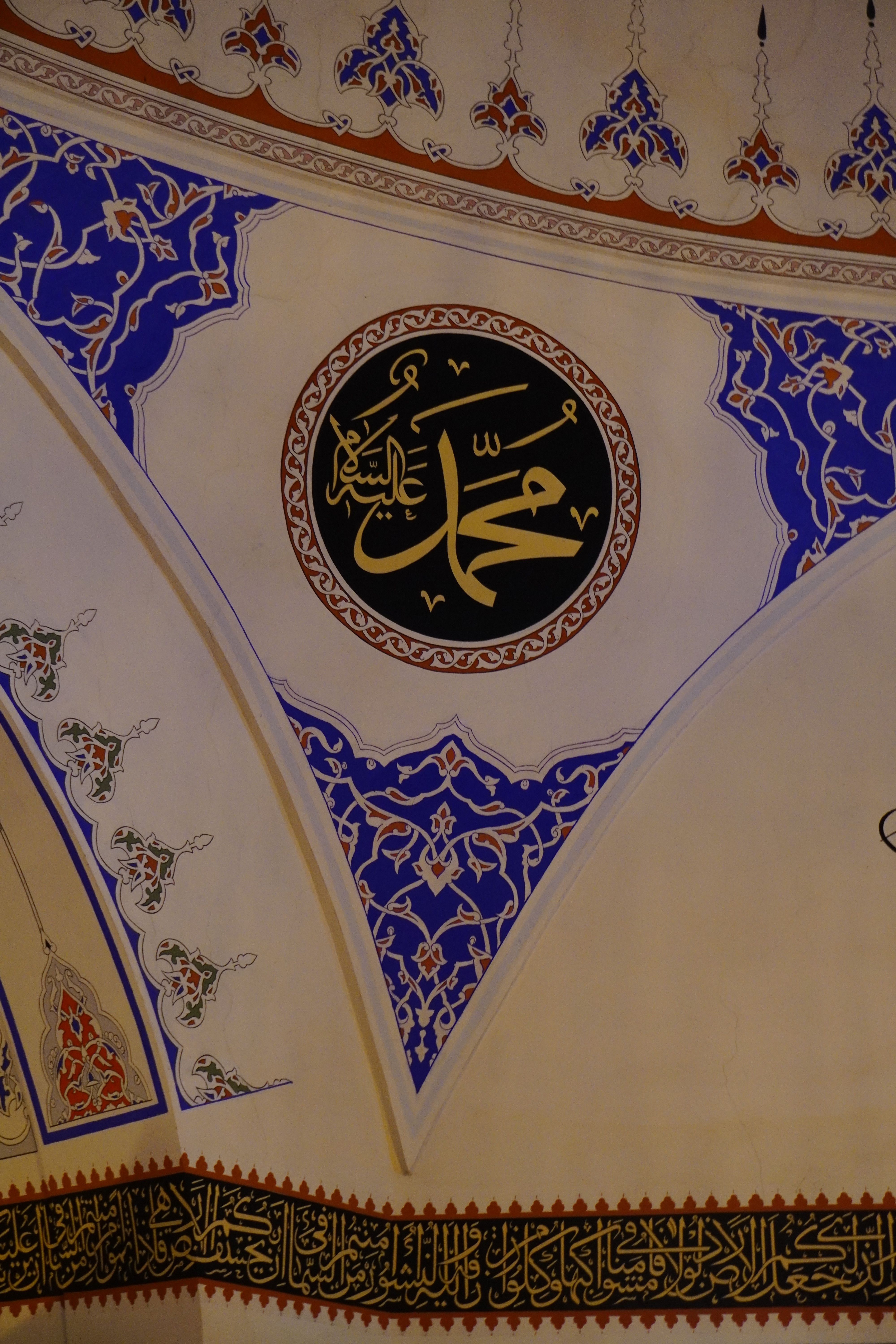 Close-up of ornate Islamic calligraphy on a mosque ceiling with vibrant blue and gold details.