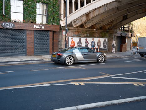 A sleek sports car parked near a bridge and urban setting, under clear daylight.