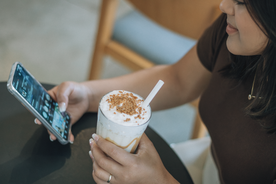 A woman is sipping iced coffee and browsing her smartphone at a cafe.