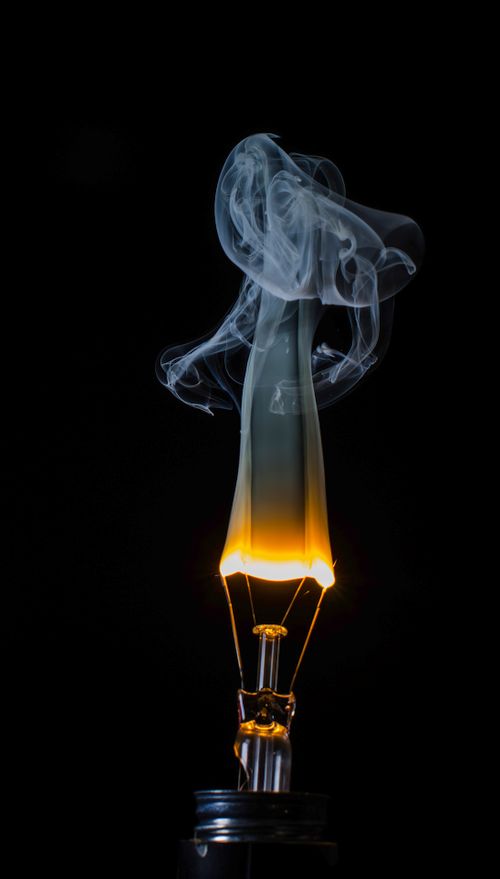 Free Artistic capture of a light bulb with mystical swirling smoke against a dark background. Stock Photo