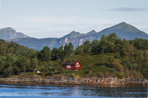Free A picturesque red cabin near a tranquil lake with mountains in the background. Stock Photo