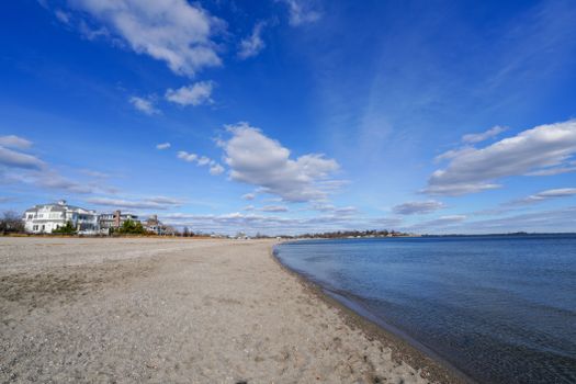 Peaceful beachfront scene with elegant houses, sandy shore, and blue sky.