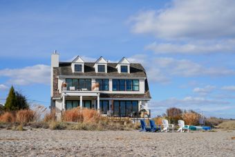Beachfront house with patio chairs among dune grasses — photo by Cara Denison on Pexels