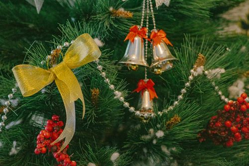 Free Close-up of a decorated Christmas tree with shiny bells, a gold bow, and red berries. Stock Photo