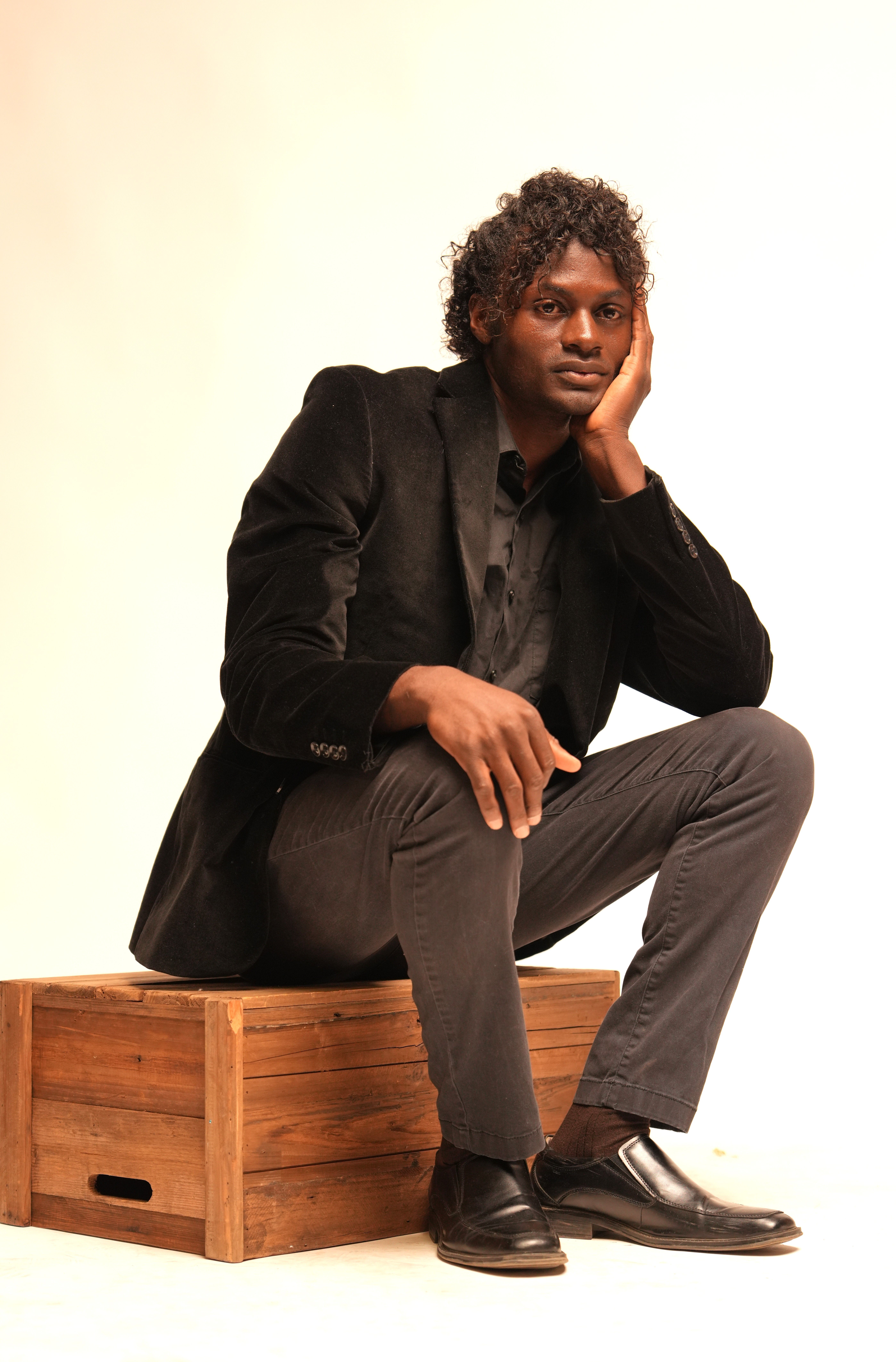 Stylish man in suit sits thoughtfully on a wooden box in a modern setting.