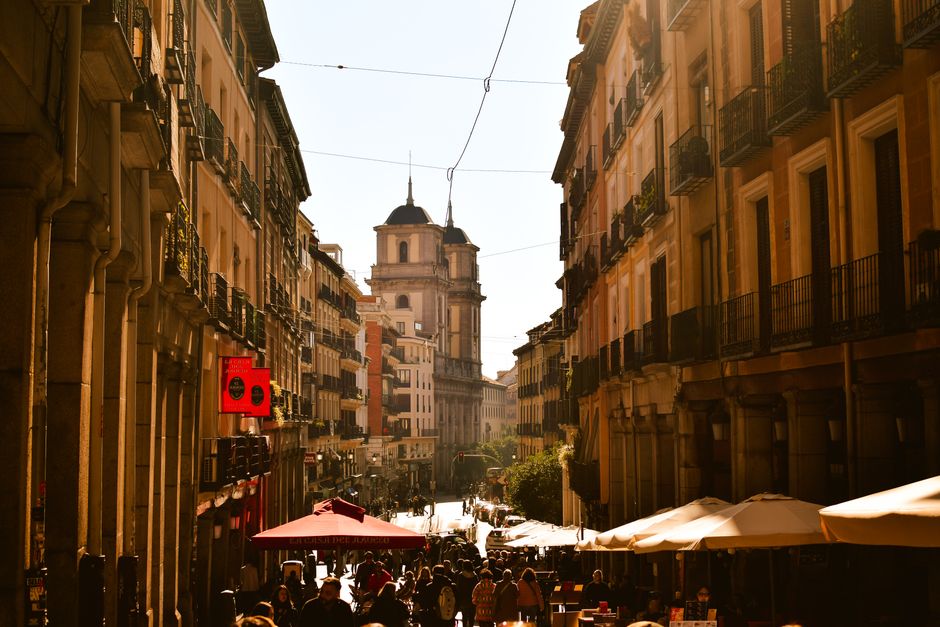 Una concurrida calle europea con arquitectura clásica y un ambiente animado bajo la cálida luz del sol de la tarde.