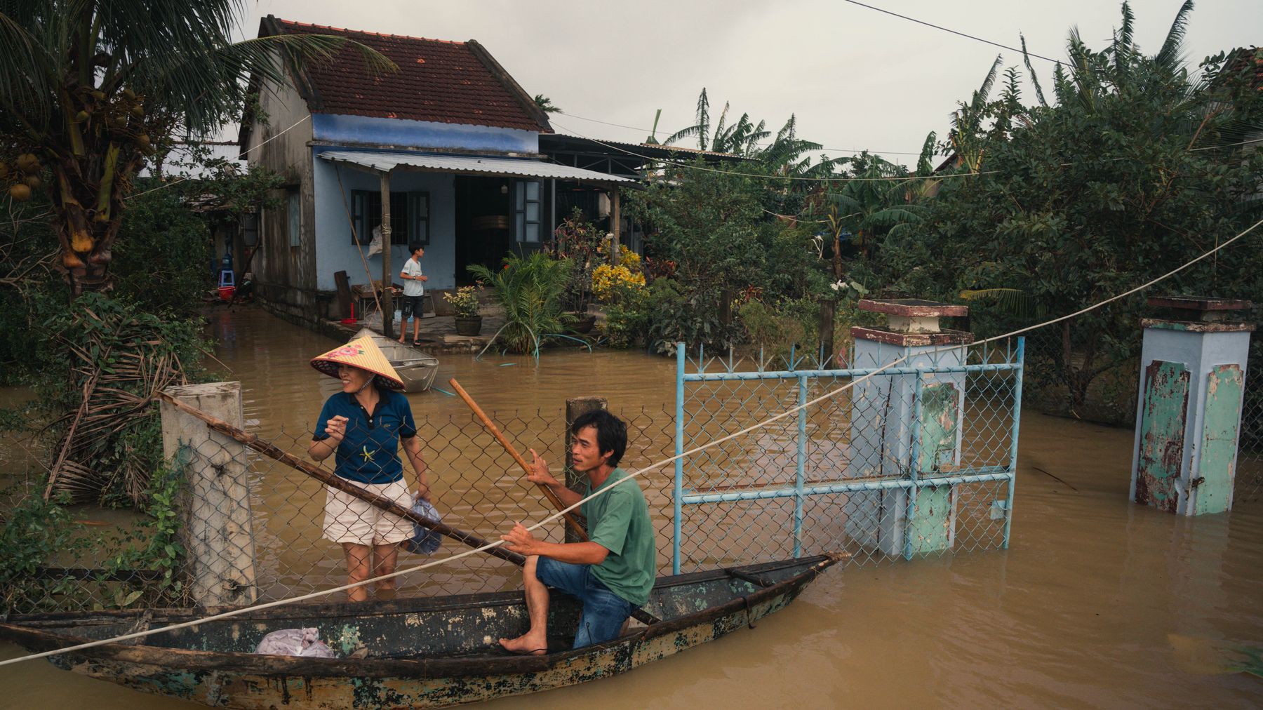 Residents navigate floodwaters in Phú Yên, Vietnam, using a small wooden boat.