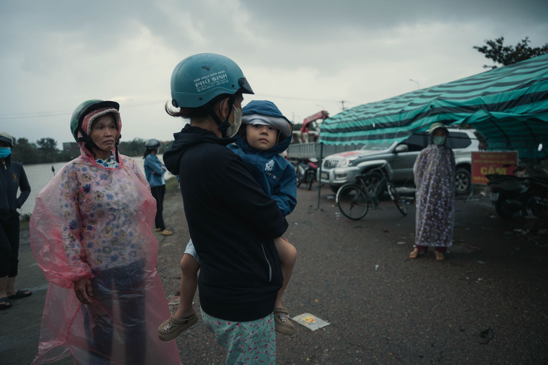 Locals in Phú Yên, Vietnam wearing raincoats and helmets during an overcast day, capturing a slice of everyday life.