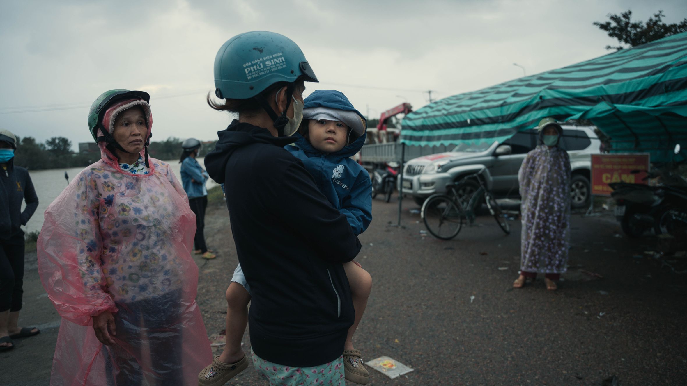 Locals in Phú Yên, Vietnam wearing raincoats and helmets during an overcast day, capturing a slice of everyday life.