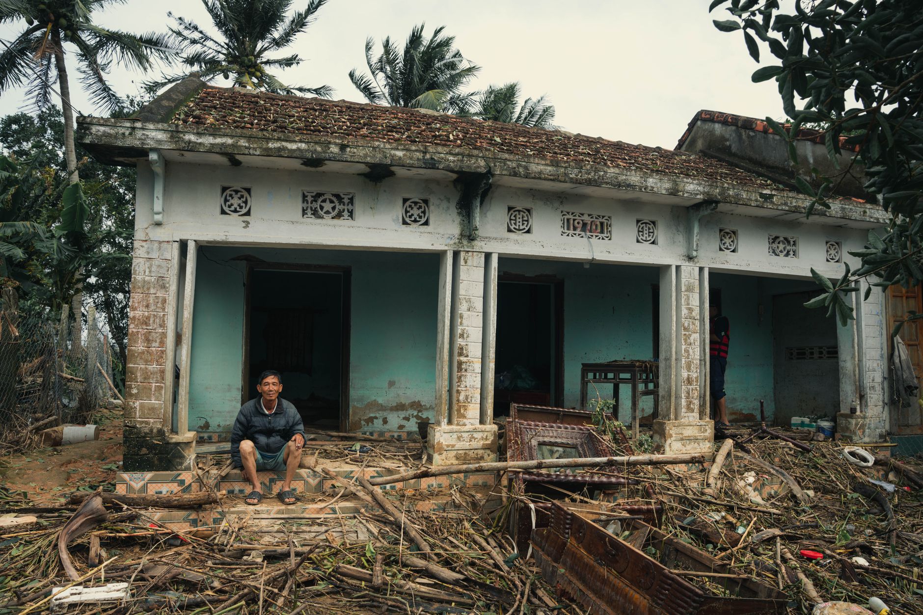 A man sits outside his flood-damaged home surrounded by debris in Phú Yên, Vietnam.