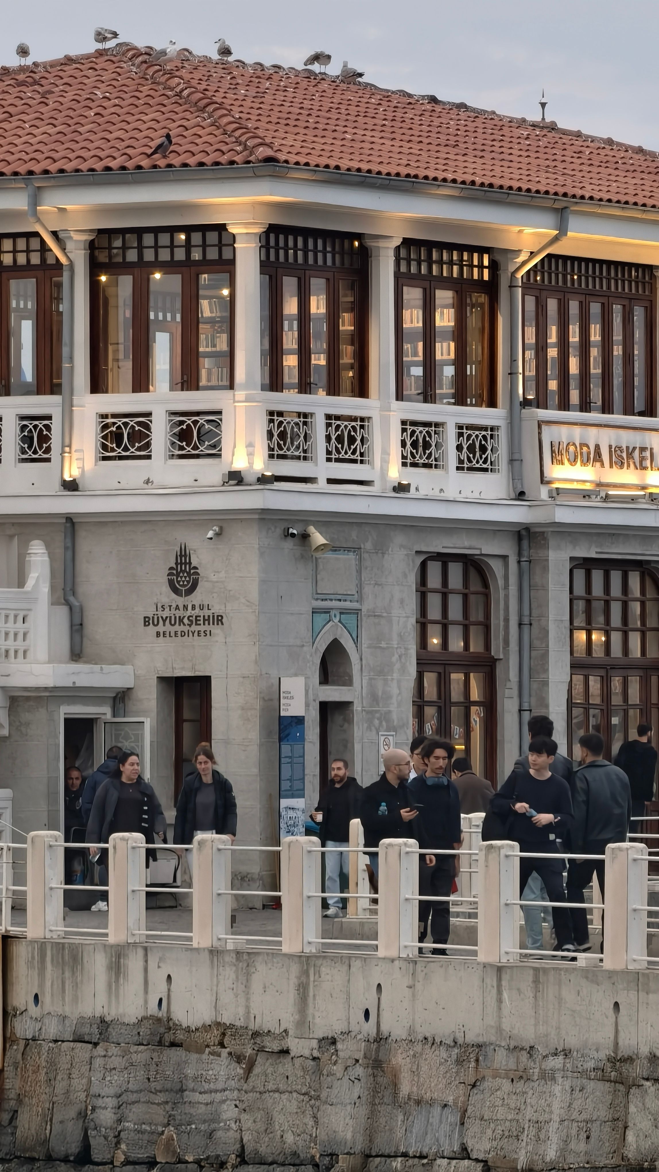 People walking by the historic Moda Pier in Kadıköy, Istanbul at dusk.