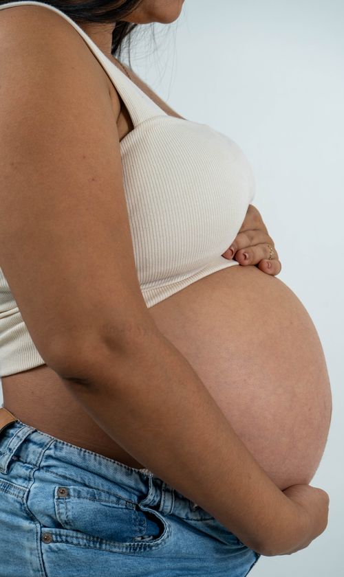 Free Side view of a pregnant woman in casual clothing holding her belly, symbolizing motherhood and anticipation. Stock Photo