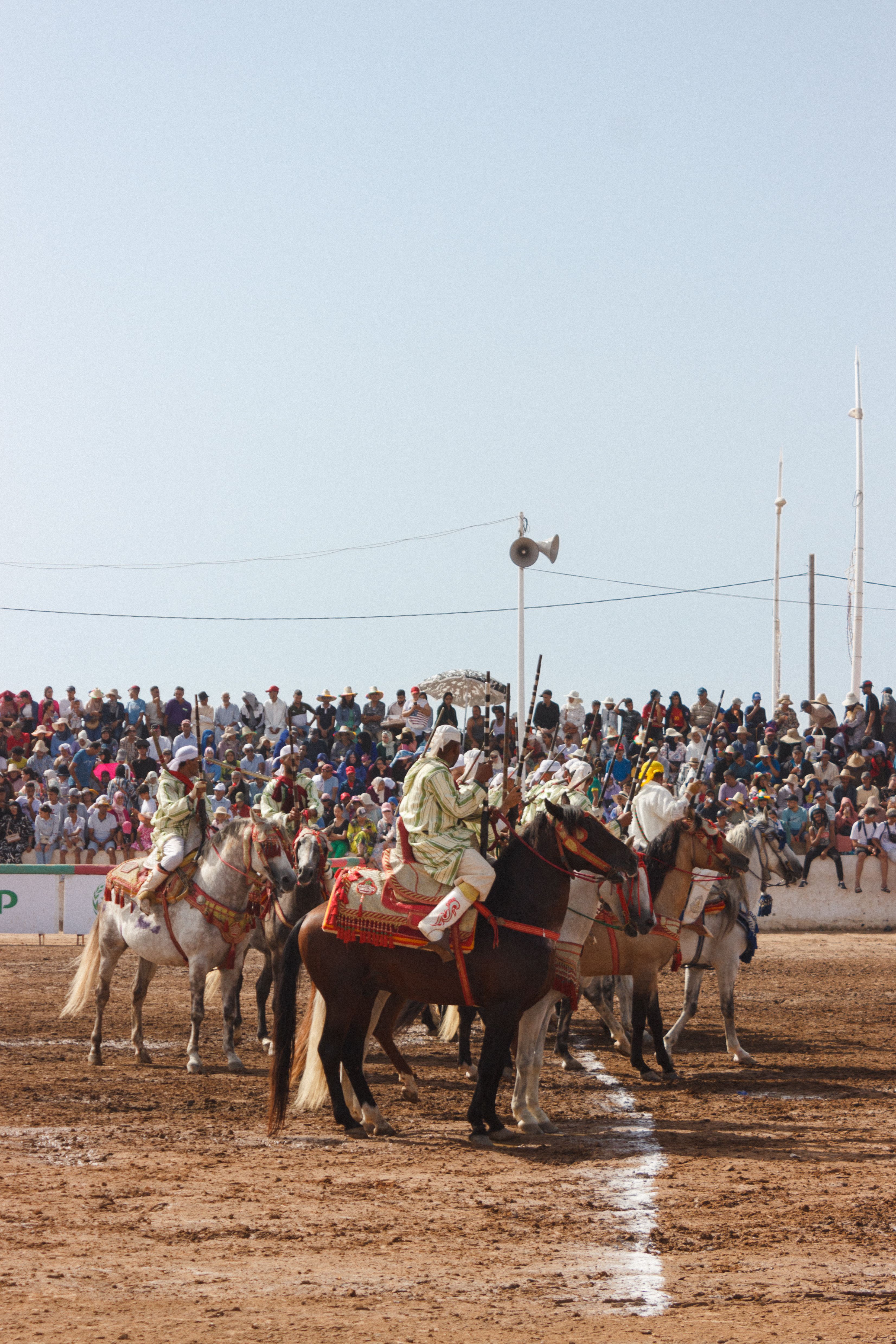 Riders in traditional attire perform in a lively horseback event before a crowd.