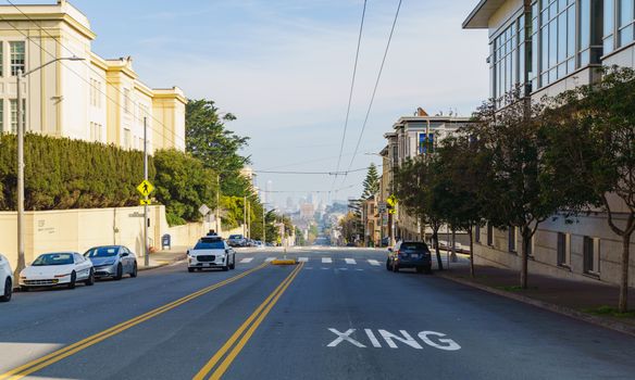 Street view of an urban neighborhood with distant city skyline under clear skies.
