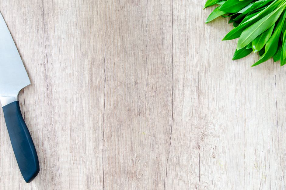 Chef knife resting beside fresh greens on a wooden worktop