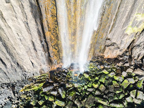 A stunning aerial view of a waterfall pouring over a rocky cliff, surrounded by moss-covered stones.