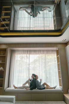 A couple enjoying wine by a large window in a modern living room with mirrored ceiling reflection.