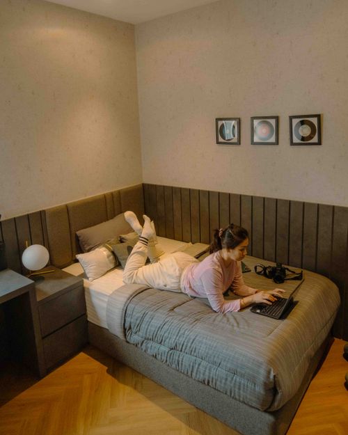 Free Woman relaxing on a bed using her laptop in a cozy bedroom setting. Stock Photo