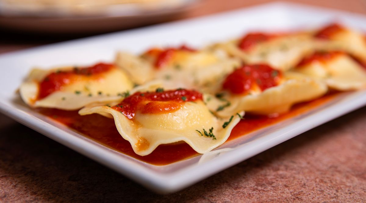 Ricotta ravioli with dollops of tomato sauce and herbs on a long white platter
