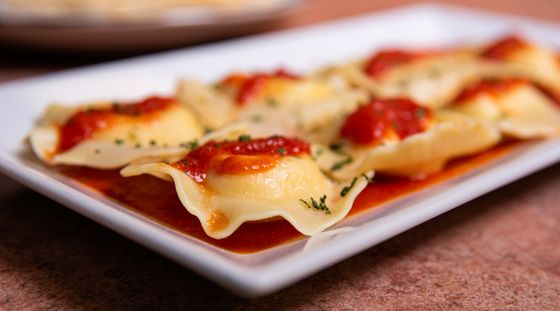 Ricotta ravioli with dollops of tomato sauce and herbs on a long white platter