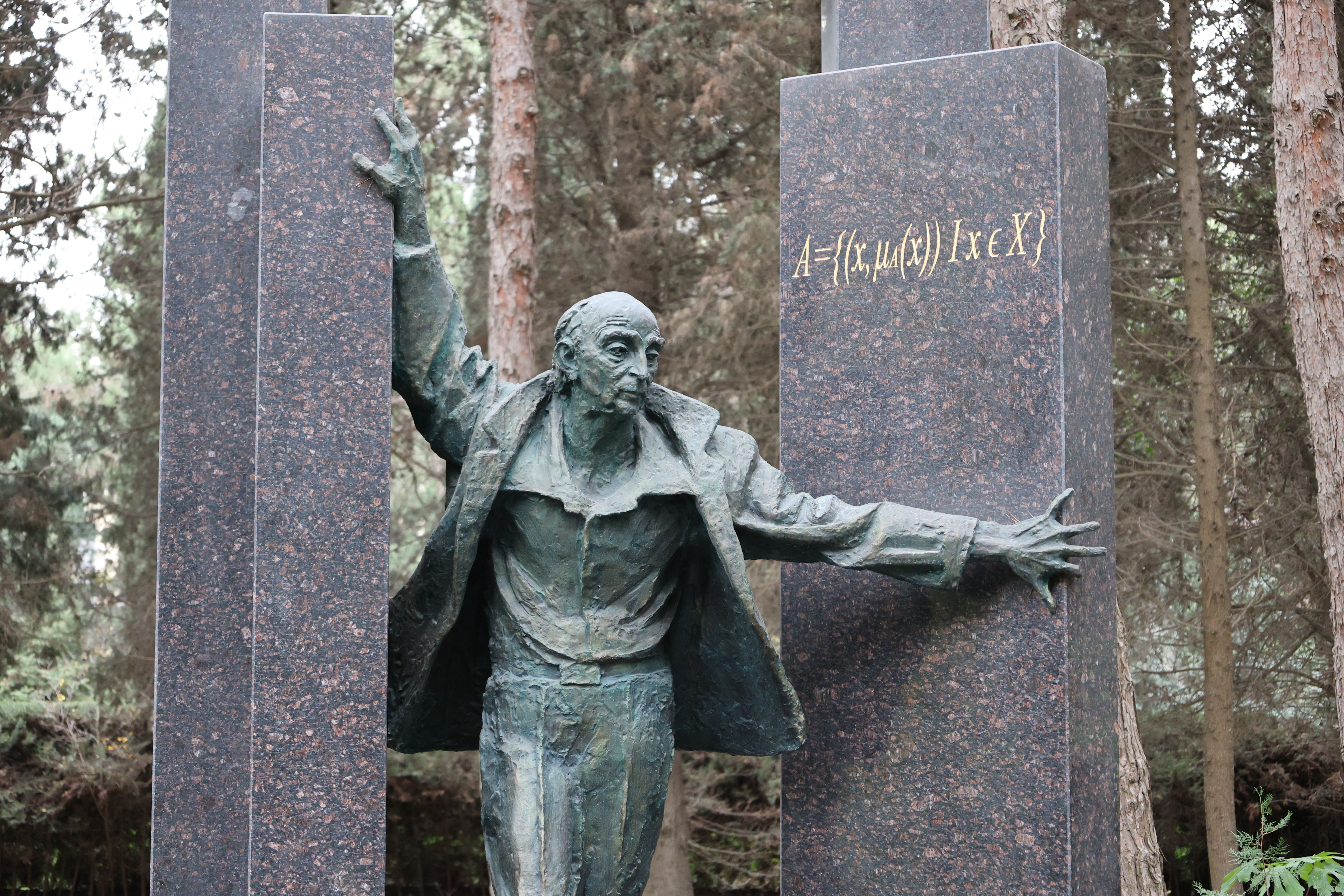 Bronze sculpture with abstract design surrounded by forest trees.