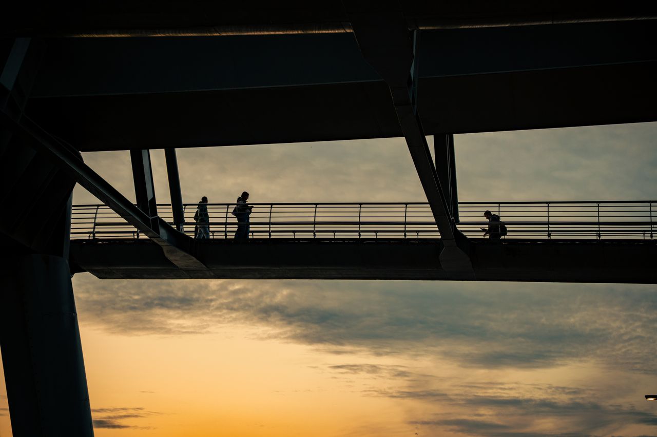 silhouettes of people walking on a bridge during a vibrant sunset