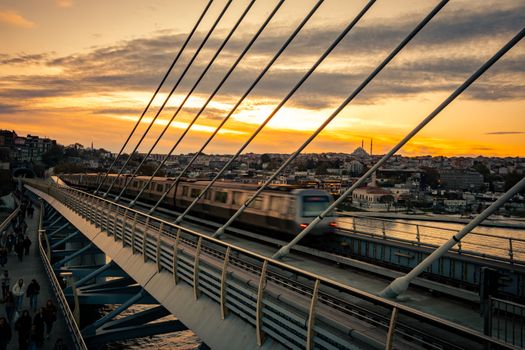 Dramatic sunset view of Istanbul Metro crossing the iconic Golden Horn Bridge in Istanbul.