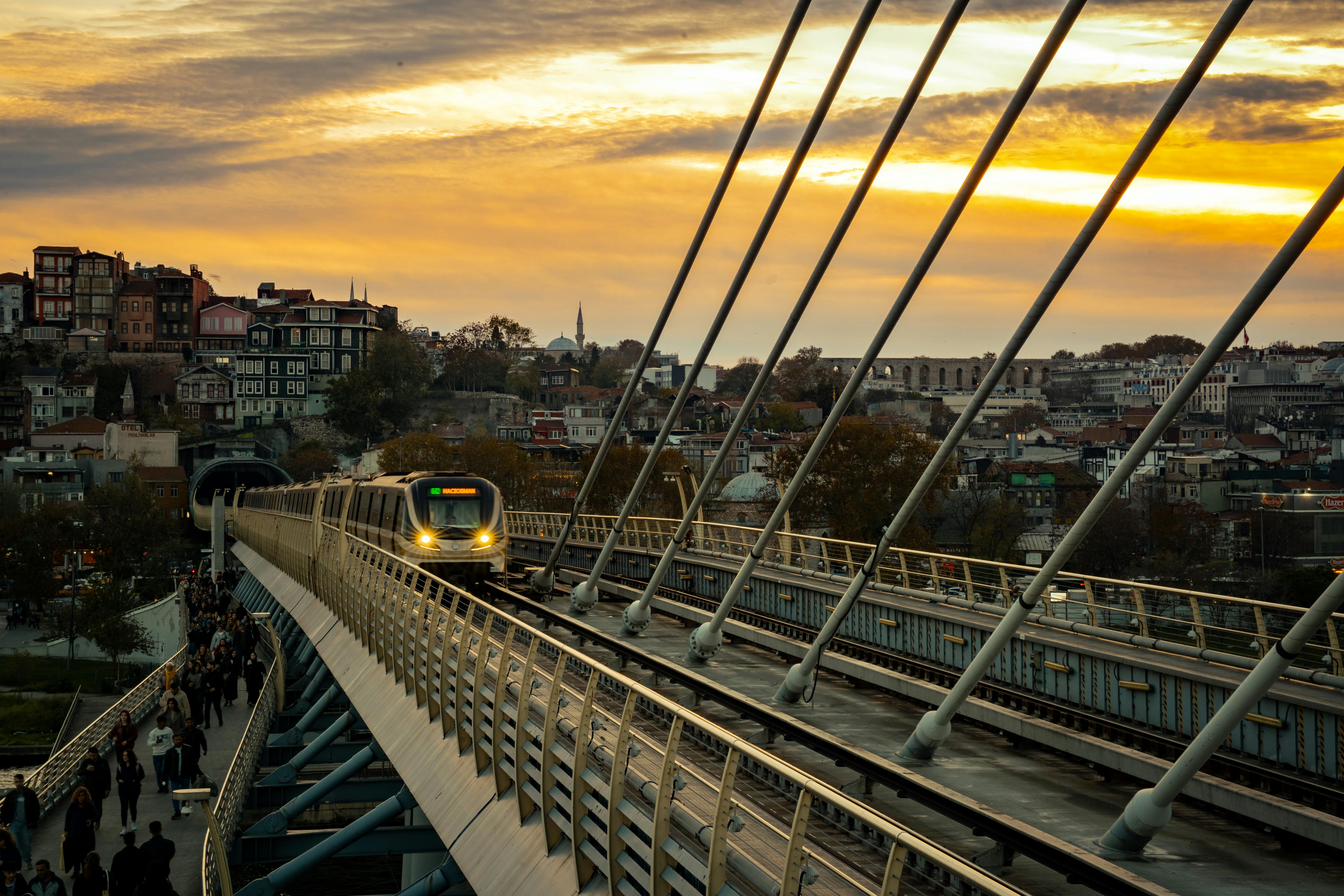 Gratuit Vue du coucher de soleil sur un train traversant le pont du métro de la Corne d'Or, avec le paysage urbain d'Istanbul en arrière-plan. Photos