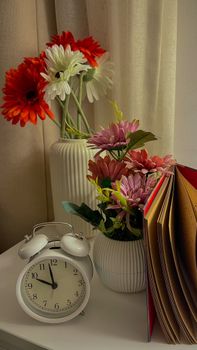 Aesthetic arrangement of flowers, clock, and open book on a table indoors.