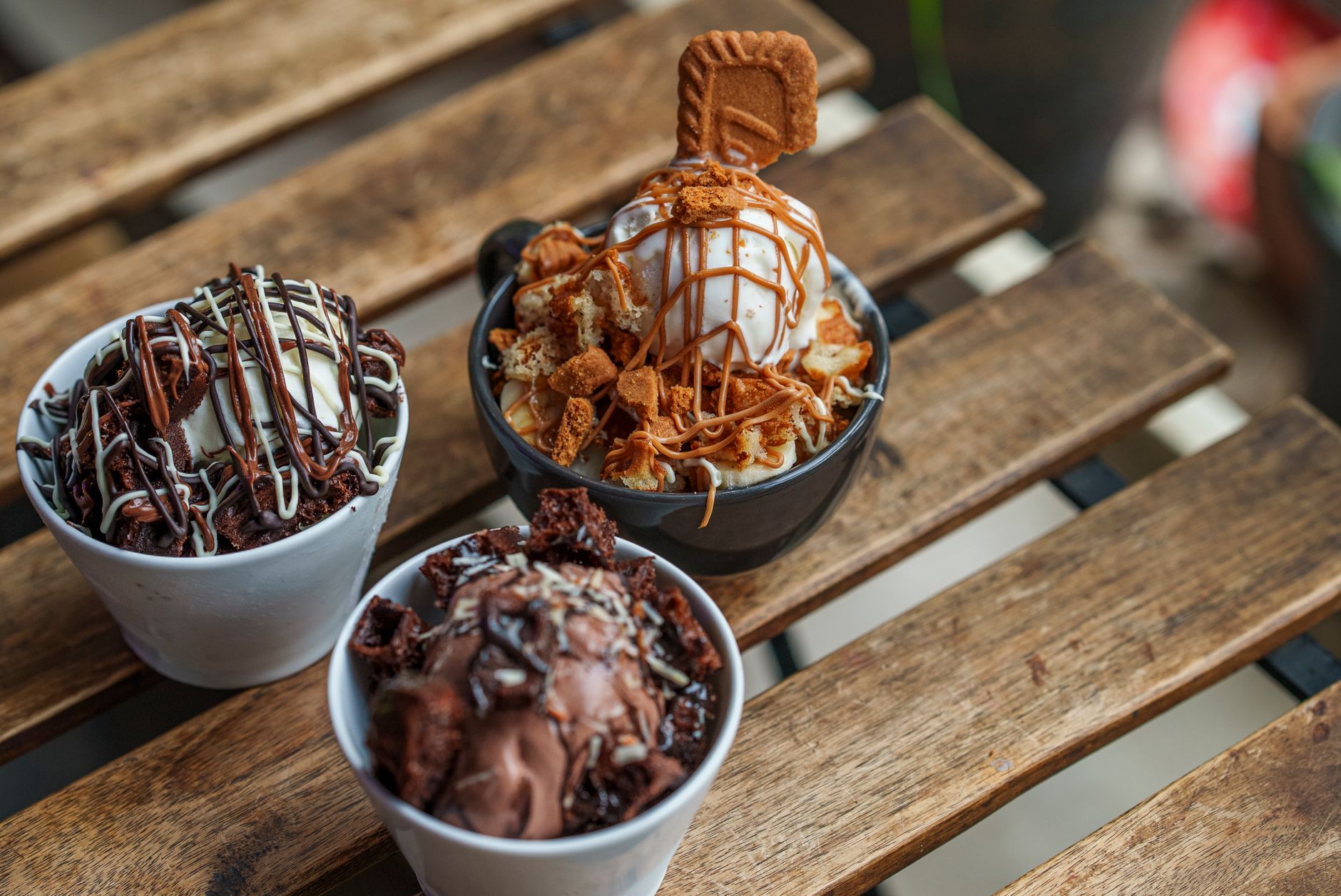 Overhead view of three ice cream desserts with various toppings on a wooden table.