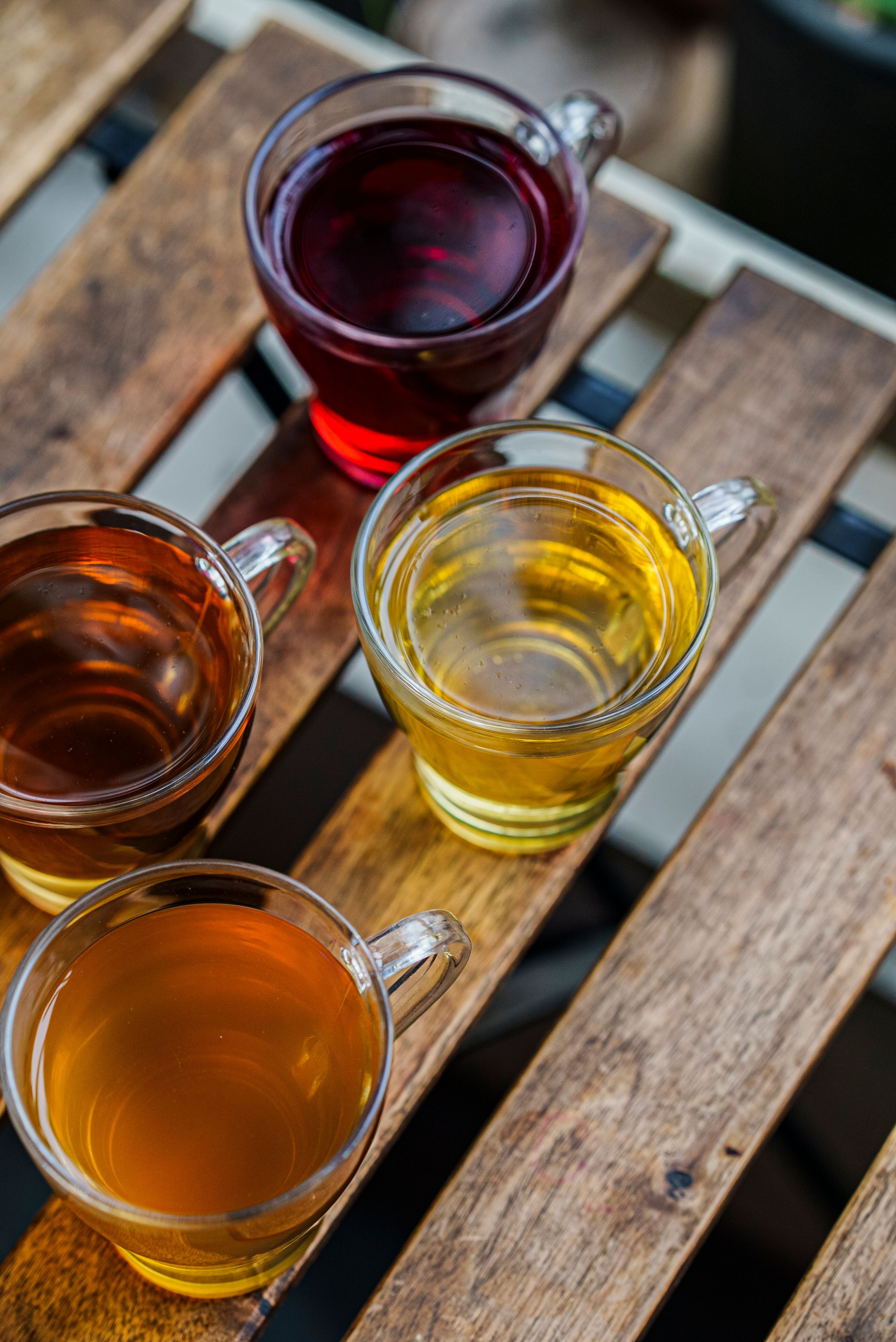 Top view of four glasses with different colored herbal teas on a wooden table, each offering distinct flavors.