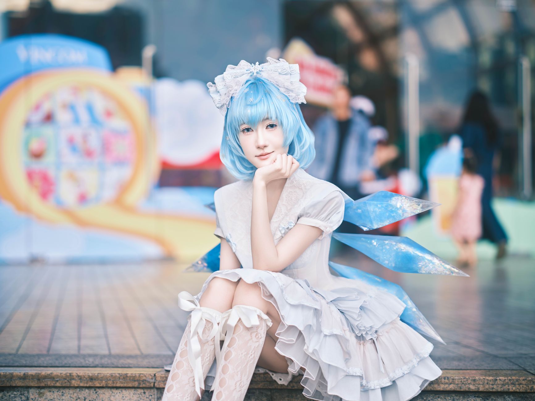 A young adult in cosplay with blue hair and wings poses outdoors.