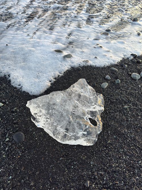 Free A piece of ice rests on a black sand beach as waves gently wash over it in Iceland. Stock Photo