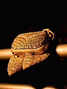Luxurious golden handbag showcased against a dark background, highlighting its intricate design.