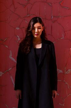 一位身着黑色外套的女性，以红色斑驳的墙壁为背景，展现出优雅时尚的肖像