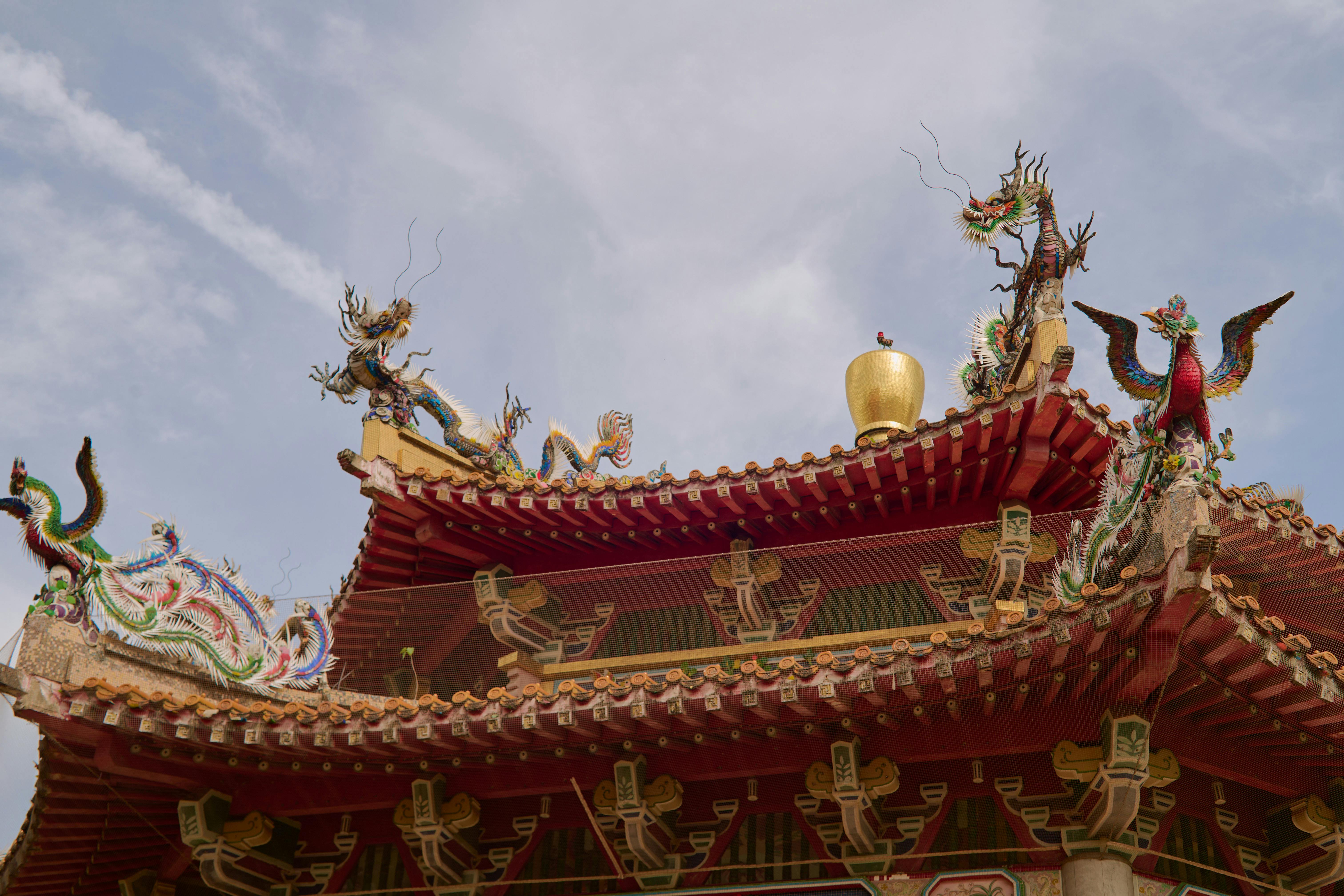 Vibrant red Chinese temple rooftop adorned with intricate dragon sculptures under a clear sky.