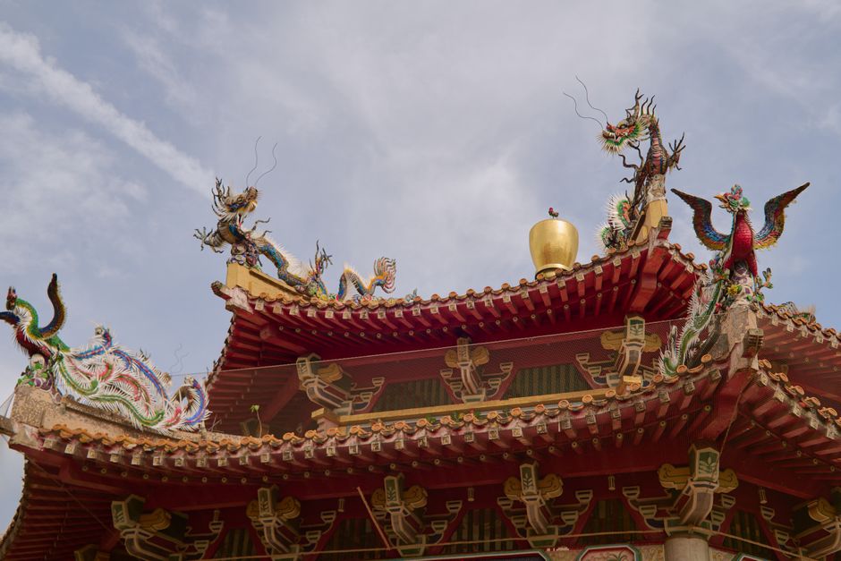 Vibrant red Chinese temple rooftop adorned with intricate dragon sculptures under a clear sky.