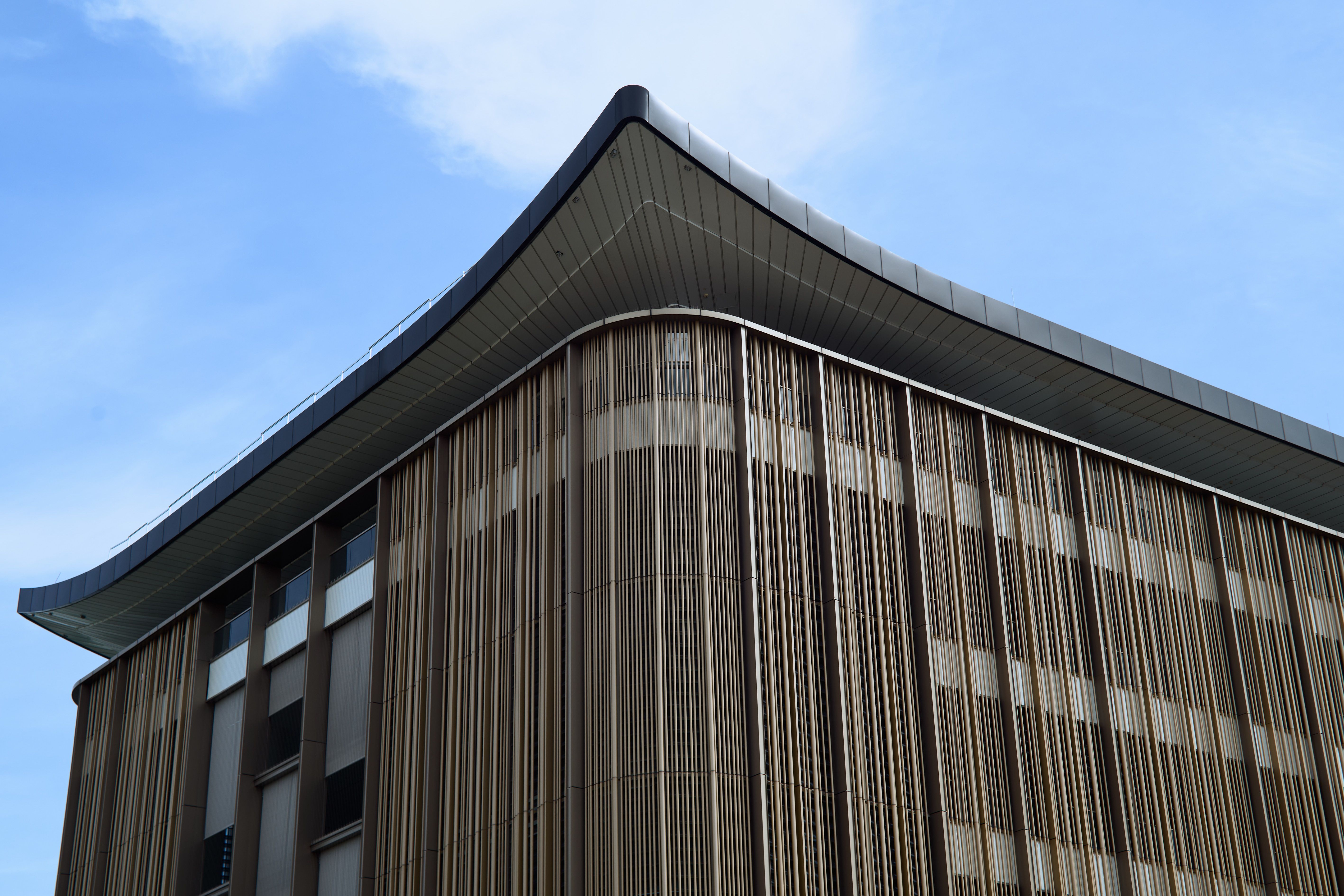Angled view of a modern building featuring vertical slats and a curved roof against a blue sky.