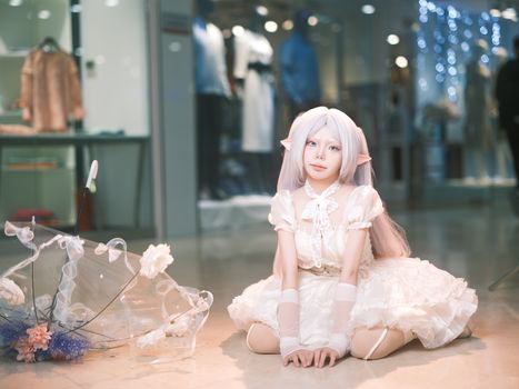 A person in elf cosplay sitting indoors, surrounded by elegant décor and lights.